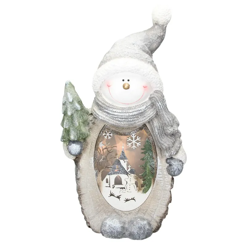 Dekorativer Schneemann mit Tannenbaum und beleuchtetem Winterdorf.