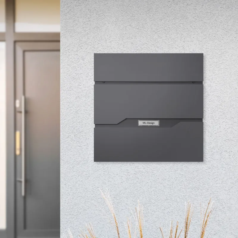 Briefkasten an einer Wand, neben einer Tür, mit dekorativen Gräsern.