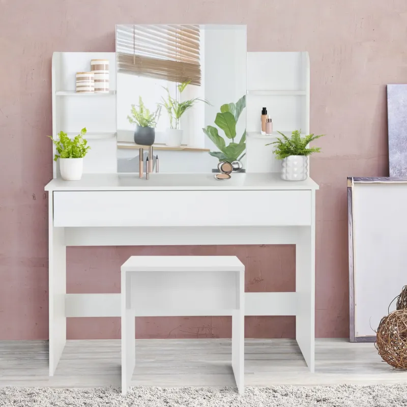 Ein weißer Schminktisch mit Pflanzen, Spiegel und Hocker vor einer rosa Wand.
