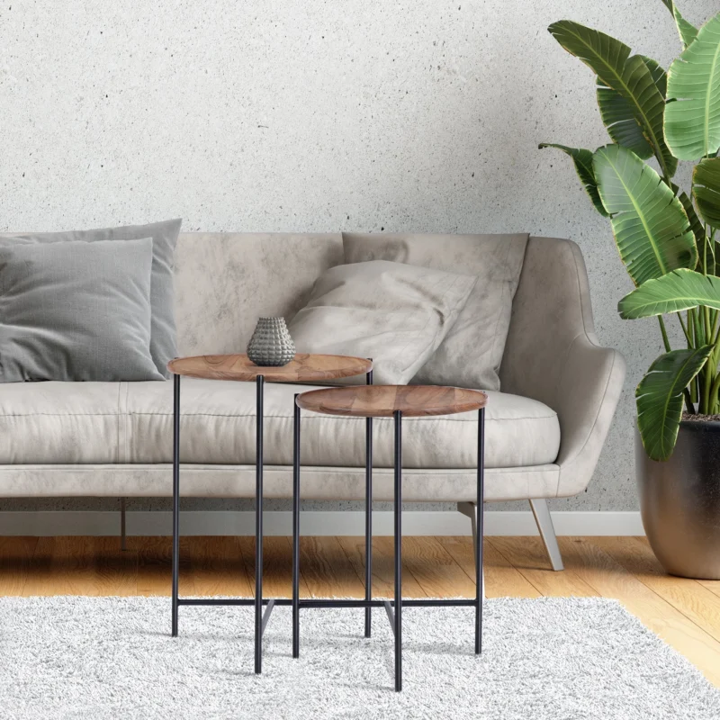 Zwei kleine Beistelltische neben einer grauen Couch vor einer Betonwand.
